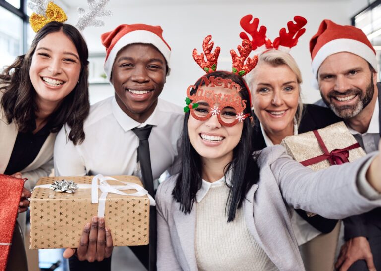 Fröhliche Mitarbeiter:innen mit Weihnachtsgeschenken bei einer Weihnachtsfeier im Büro.