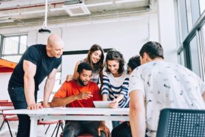 Junger Büroangestellter erklärt seinen Mitarbeitenden etwas im Büro; als Symbol für Peer Learning.