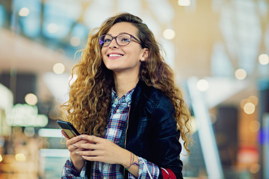 Junge Frau lächelt und hält hier Smartphone, nachdem sie eine gute Customer Experience hatte.