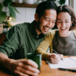 Two smiling people are learning a language together in their home.