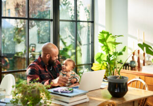 Ein Vater arbeitet mit seinem Baby im Arm im Homeoffice, da er flexible Arbeitsregelungen hat.