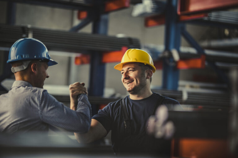 Young happy worker and manager giving each other manly greet at steel mill