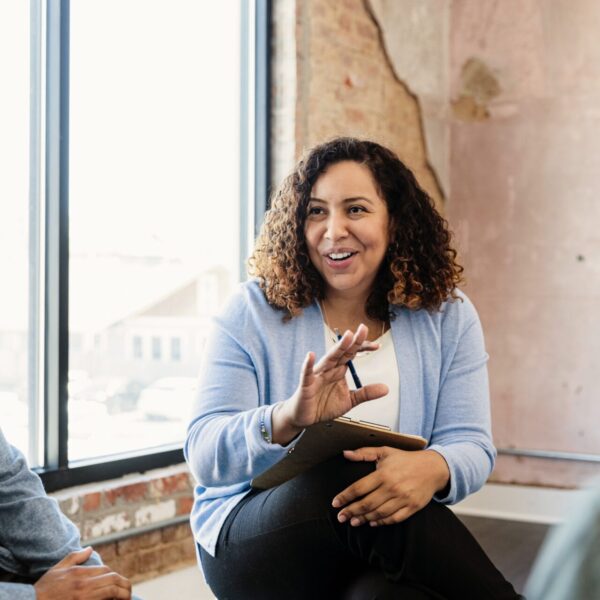 In the staff meeting, the mid adult female manager smiles and gestures as she presents a new idea to the unrecognizable employees.